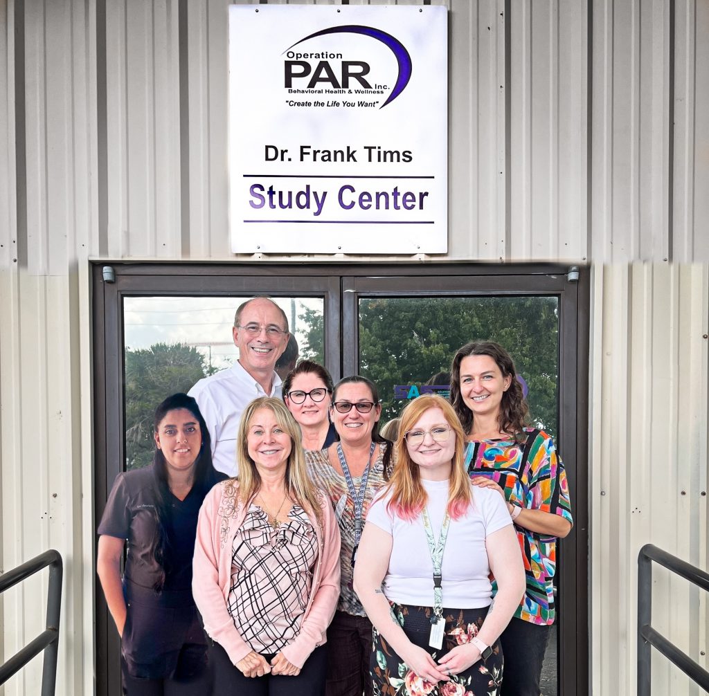 The PAR Team smiling in front of a sign on their office door that reads Operation PAR, Dr. Frank Tims, Study Center. 