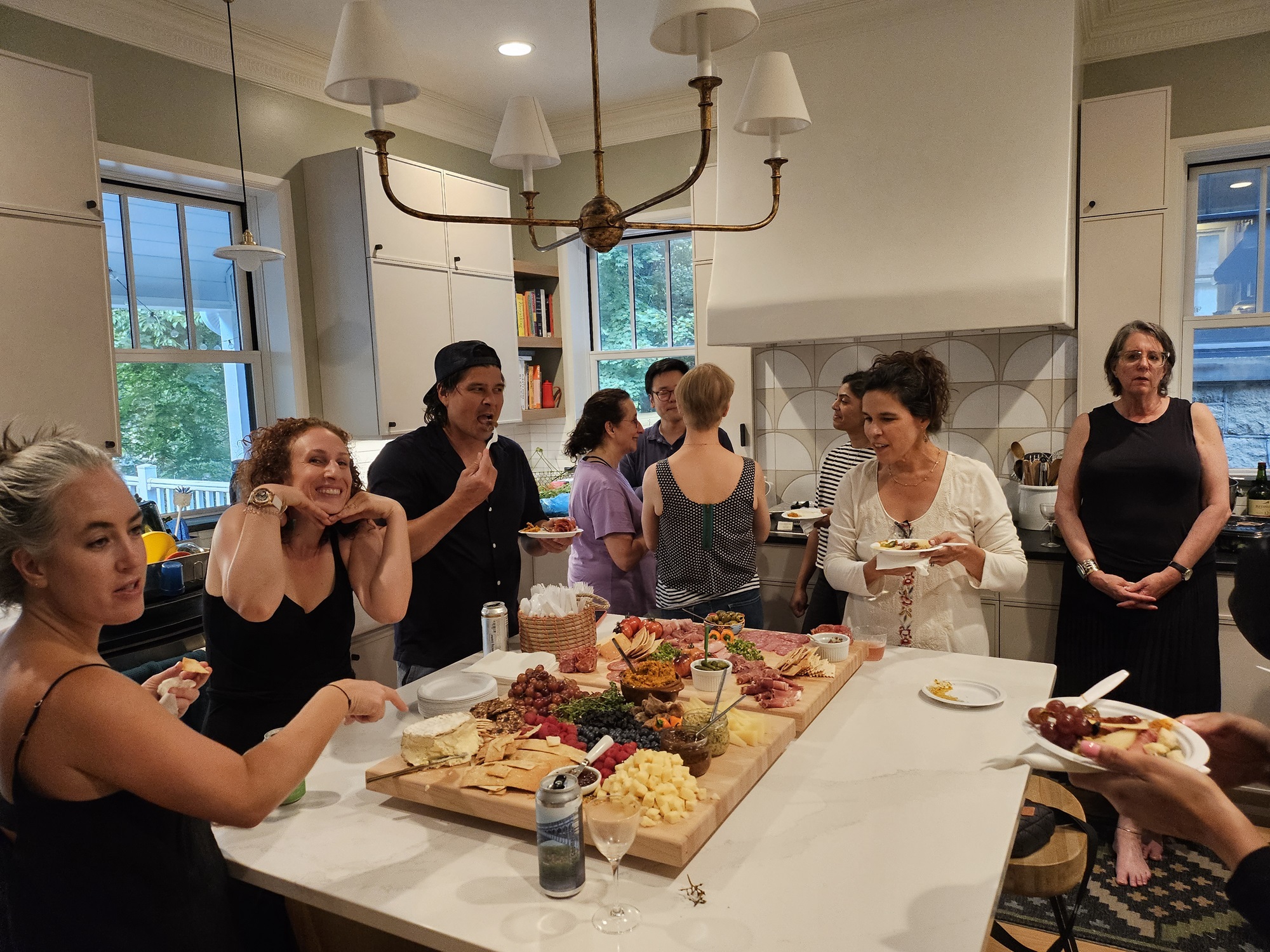 Group of people around a large platter of food in a kitchen, socializing