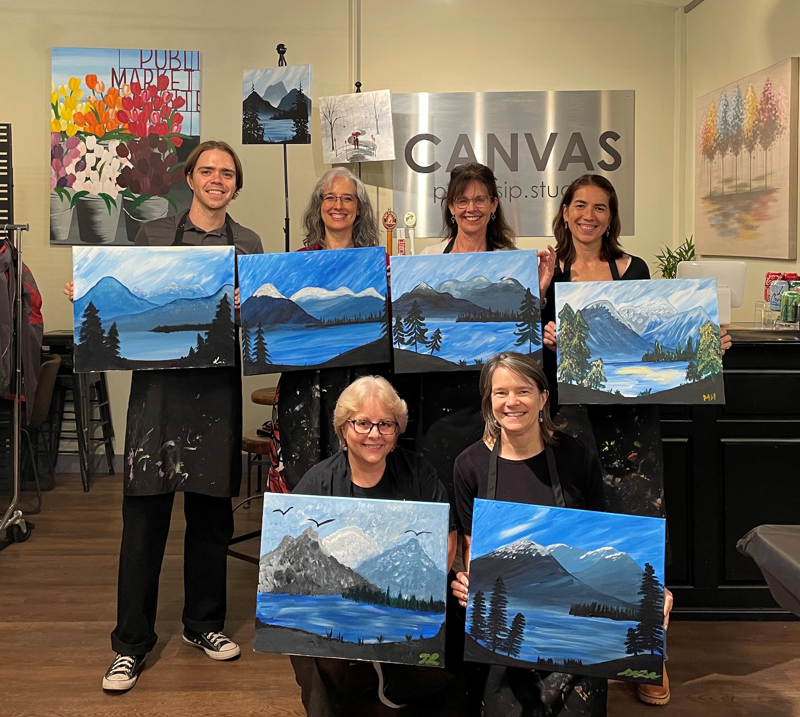 PNW Node team holding up their landscape paintings from a "Paint & Sip" session